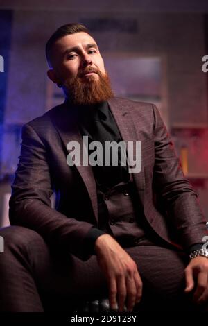 bell'uomo giovane in un tuxedo seduto al buio camera con abbigliamento alla moda per le serate di festa Foto Stock