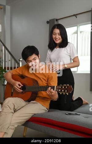 Boyfriend sta suonando una chitarra alla sua bella ragazza sul divano in soggiorno. Foto Stock