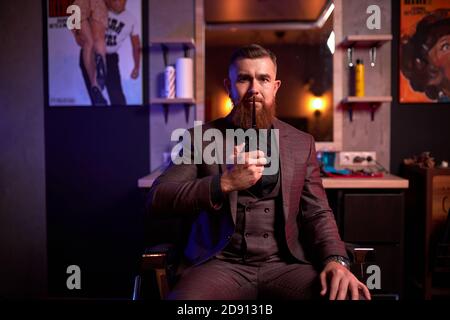 lo stylist professionale dei capelli è pronto per tagliare i vostri capelli o barba, maschio in abito sul posto di lavoro, in posa in stanza buia Foto Stock