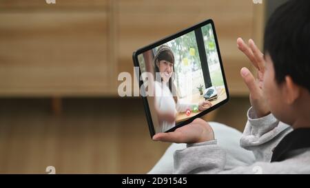 Ripresa di una giovane donna seduta sul divano in salotto e che parla con l'amico tramite videochiamata. Foto Stock