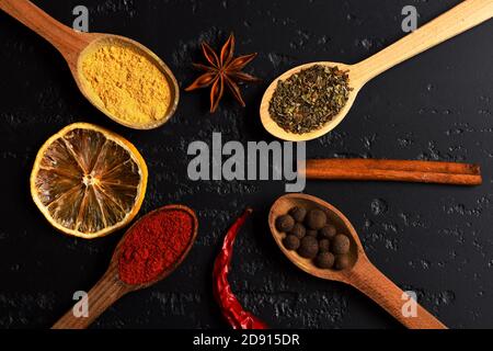 Set di spezie su sfondo di legno grigio scuro. Concetto di arte alimentare. Composizione del condimento, vista dall'alto. Cucchiai di legno con paprika, curcuma, erbe e pepe di cannella, anice, fetta di arancia secca e peperoncino. Foto Stock