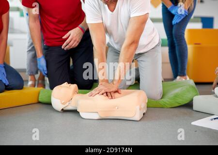 Giovane maschio che pratica CPR primo soccorso su un manichino in presenza di persone, al chiuso Foto Stock