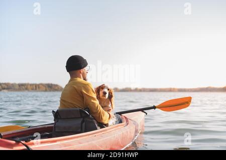 Uomo con un cane in canoa sul lago. Giovane uomo con spaniel in una barca di fila di kayak, tempo libero attivo con animali domestici, compagnia, cani d'avventura Foto Stock