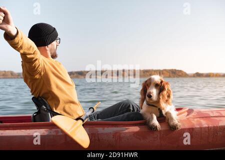 Kayak con cani: L'uomo si allunga seduto in una barca a remi sul lago accanto al suo spaniel. Riposo attivo e avventure con gli animali domestici, a cavallo di una canoa con il cane Foto Stock