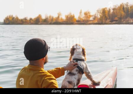 Kayak con cani: L'uomo si siede in una barca a remi sul lago accanto al suo spaniel. Riposo attivo e avventure con gli animali domestici, a cavallo di una canoa con il cane Foto Stock