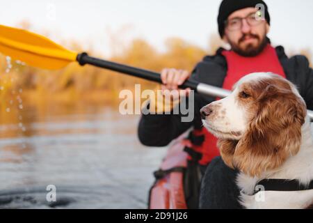 Uomo che canottava con il suo cane spaniel, bel tempo autunnale. Andare in kayak con cani sul fiume, animali domestici attivi, cane felice e proprietario su un adve Foto Stock