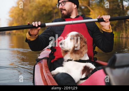 Uomo felice canottaggio con il suo cane spaniel, sole stagione autunnale. Andare in kayak con cani sul fiume, animali attivi, cani sani e proprietario Foto Stock