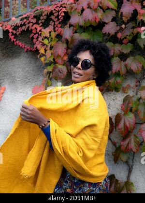 Ritratto verticale di un'elegante donna afro-americana in piedi fronte delle foglie d'autunno Foto Stock