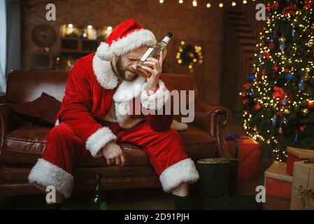 Babbo Natale cattivo con alcol sul divano, sbornia Foto Stock