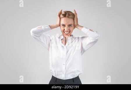 Stressato dipendente d'ufficio che si aggrappava la testa, sentendosi arrabbiato o disperato su sfondo grigio chiaro studio Foto Stock