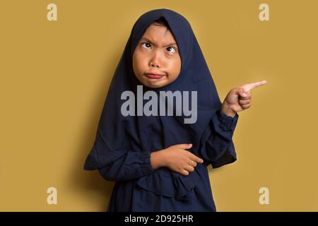 asian ragazza musulmana piccola che indossa hijab con l'espressione bizzarra e. punta la mano sullo spazio vuoto Foto Stock