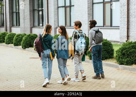 Vista posteriore di ragazzi sorridenti con zaini che camminano in città via Foto Stock