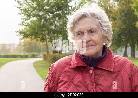 Donna anziana sorridente su sfondo autunno natura con spazio di copia. Ritratto su felice anziana donna nel parco cittadino con alberi d'autunno. Felice e sano pensionato Foto Stock