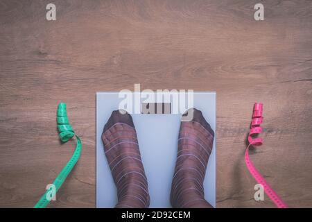 Piedi donna in calze in piedi su scale e sfondo di legno per la copia spazio. Gambe femmine in calza su bilance e nastri di misurazione. Concetto di dieta. Foto Stock