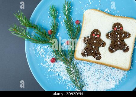 Pane tostato, decorato con pan di zenzero glaze, ribes rosso congelato, ramo di abete rosso su un piatto blu, su uno sfondo scuro. Natale, anno nuovo. Fest Foto Stock