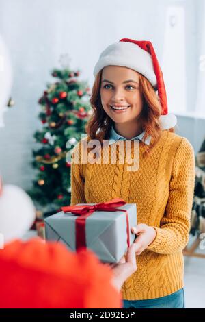 fuoco selettivo della donna felice in cappello di santa che prende il regalo scatola da marito Foto Stock