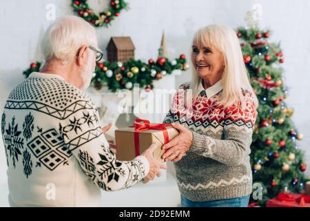 donna anziana che presenta la scatola del regalo con la decorazione di natale sullo sfondo Foto Stock