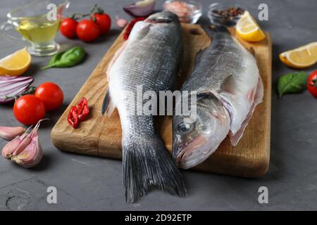 Due frutti di mare grezzi con ingredienti e condimenti come basilico, limone, sale, pepe, pomodori ciliegini e aglio su tavola di legno su sfondo scuro Foto Stock