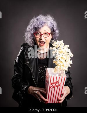 Primo piano ritratto di bella donna anziana che tiene popcorn sopra uno sfondo grigio Foto Stock