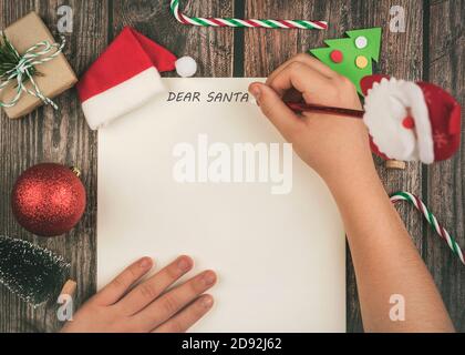 Buon Natale.Natale concetto sfondo. Le mani del bambino scrivono la lettera a babbo natale su sfondo di legno Foto Stock