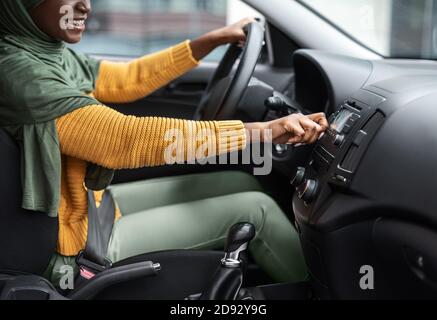 Donna musulmana nera irriconoscibile che attiva il volume nell'audio dell'auto sistema Foto Stock