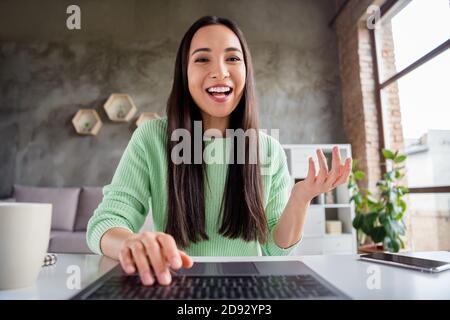 Primo piano foto di positivo ragazza cinese seduta scrivania utilizzare il laptop hanno la comunicazione di trasmissione che parla notizie in casa in interni Foto Stock