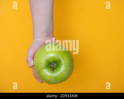 Un bambino tiene in mano una mela verde sfondo giallo Foto Stock