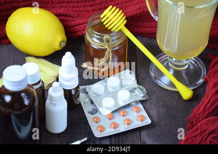 sanità, medicina tradizionale e concetto di influenza - tazza da tè con limone, zenzero, miele e pillole su tavola di legno. compresse, pillole, sciroppi di tosse, nasale Foto Stock
