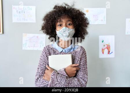 Carino alunno della piccola scuola ragazza capretto africana indossa maschera di faccia in piedi in classe. Foto Stock