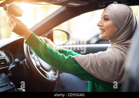 Donna musulmana felice che guida da sola regolando lo specchietto retrovisore Foto Stock