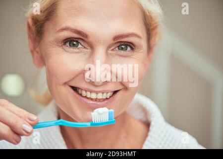 Ritratto di felice donna caucasica di mezza età con spazzolino in mano guardando la macchina fotografica e sorridendo. Concetto di bellezza, cura della pelle e cosmetologia Foto Stock