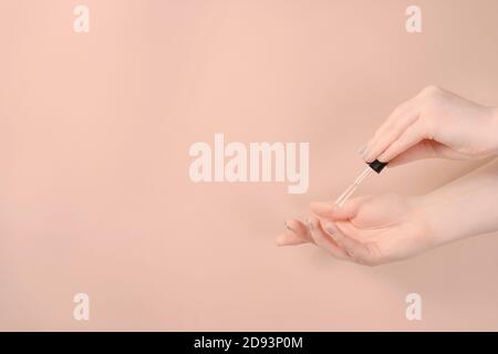 Donna con manicure pastello ha usato siero che cade sulla sua mano su sfondo beige. Cura della pelle e concetto di bellezza. Vista frontale con spazio per la copia Foto Stock