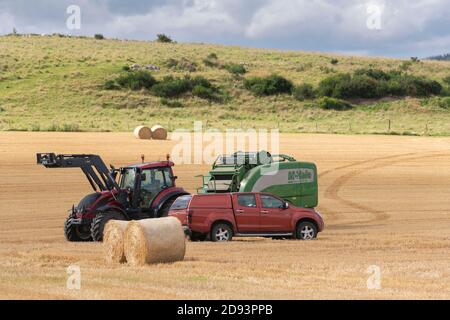 Un pick-up si trova accanto a un trattore e a una pressa McHale Durante le operazioni di raccolta ad Aberdeenshire Foto Stock