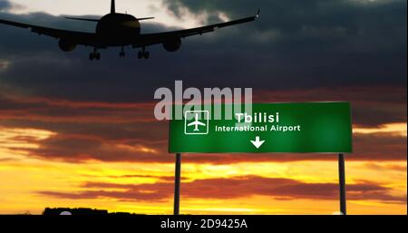 La silhouette dell'aereo atterra a Tbilisi, Georgia. Arrivo in città con cartello con la direzione dell'aeroporto e tramonto sullo sfondo. Viaggio e trasporto conce Foto Stock