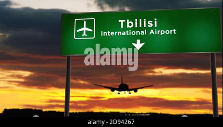 La silhouette dell'aereo atterra a Tbilisi, Georgia. Arrivo in città con cartello con la direzione dell'aeroporto e tramonto sullo sfondo. Viaggio e trasporto conce Foto Stock