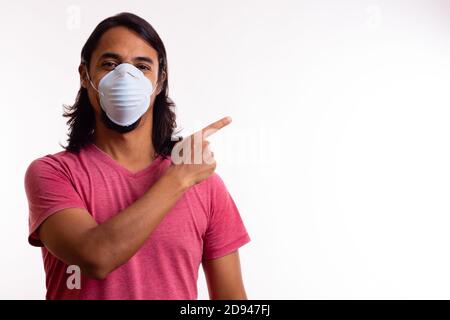 Giovane felice latino con maschera medica su sfondo bianco. Spazio di copia. Concetto di coronavirus. Foto Stock