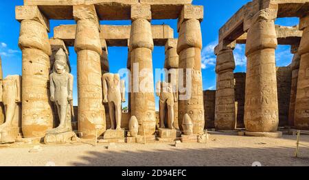 Statue del re Ramesse II nel primo cortile del tempio di Luxor. Le corone di molte delle figure si siedono a terra accanto a loro Foto Stock