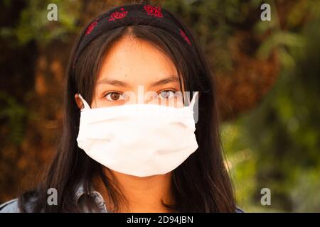 Donna ispanica che indossa maschera sulla strada vicino alberi e. natura Foto Stock