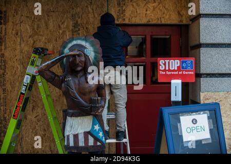 Washington, Stati Uniti. 2 Nov 2020. L'appaltatore della costruzione sale l'entrata di un commercio, con una scultura dei nativi americani in piedi vicino, in preparati Foto Stock