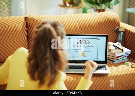 Visto da dietro la donna con certificato elettronico di laurea sullo schermo del laptop che gioisce a casa in giornata di sole. Foto Stock