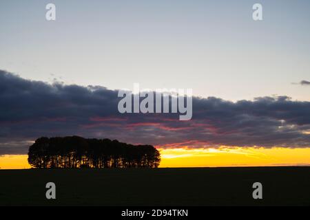 Banda di nuvole di pioggia al tramonto sulla campagna del cotswold con alberi a profilo. Cotswolds, Gloucestershire, Inghilterra Foto Stock