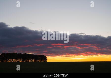 Banda di nuvole di pioggia al tramonto sulla campagna del cotswold con alberi a profilo. Cotswolds, Gloucestershire, Inghilterra Foto Stock