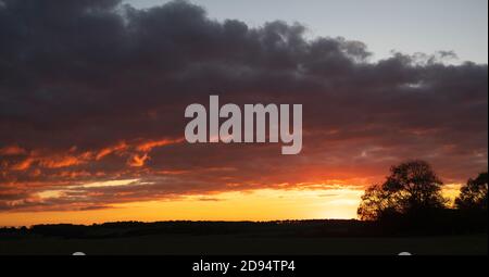 Banda di nuvole di pioggia al tramonto sulla campagna del cotswold con alberi a profilo. Cotswolds, Gloucestershire, Inghilterra Foto Stock