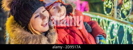 Piccolo ragazzo e sua madre con sparklers vicino all'abeto gigante e illuminazione di Natale sul mercato di Natale. Vacanze di Natale su BANNER fiera, FORMATO LUNGO Foto Stock