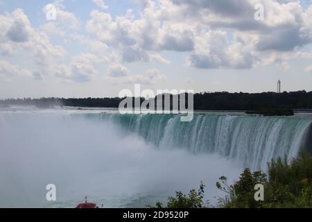 Una vista delle cascate del Niagara che mostra la nebbia proveniente da il fondo con un cielo blu nuvoloso sopra Foto Stock