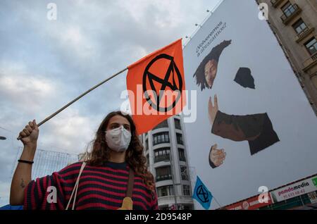 Un attivista che indossa una maschera facciale tiene una bandiera di ribellione per l'estinzione durante la manifestazione.durante la terza ribellione internazionale, il movimento di ribellione per l'estinzione ha bloccato Gran Vía Street a Madrid per protestare contro le conseguenze dell'aumento del livello del mare. Il movimento, che porta un panno blu di 150 metri quadrati da piazza Callao a piazza Spagna, attraversa via Gran Vía per rendere visibile il crescente numero di persone colpite dall'aumento del livello del mare, causato dal cambiamento climatico. Questo atto, sotto il nome di 'noi affondare' ha rappresentato l'enorme numero di morti a causa dell'aumento del livello del mare. Foto Stock