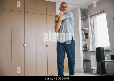 Uomo anziano che preme sul gomito per allungare il braccio Foto Stock