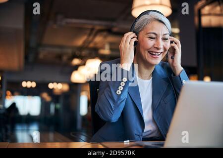Donna allegra che indossa le cuffie con l'uso del notebook al lavoro Foto Stock