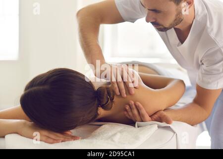 Giovane massaggiatore in centro fisioterapico massaggiando la spalla della donna, alleviando il dolore e rilassando i muscoli Foto Stock