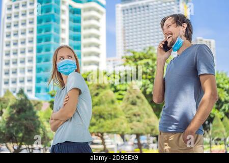 Concetto di allontanamento sociale. Un uomo in strada viola la distanza sociale in linea, indossa una maschera in modo errato e parla su uno smartphone Foto Stock